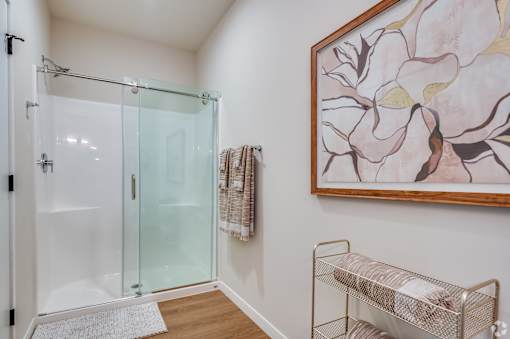 A bathroom with a glass shower door and a painting on the wall.