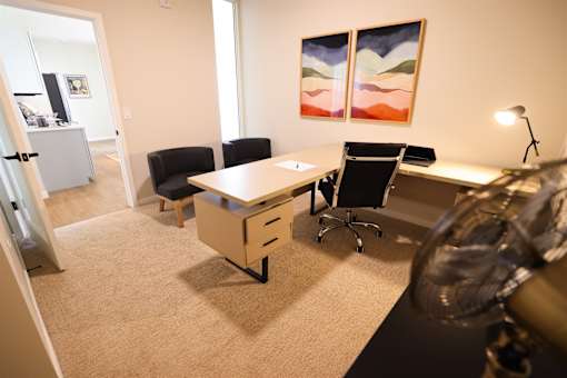 A room with a desk, chairs and a painting on the wall.