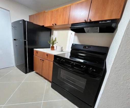 A black oven and fridge in a kitchen with wooden cabinets.
