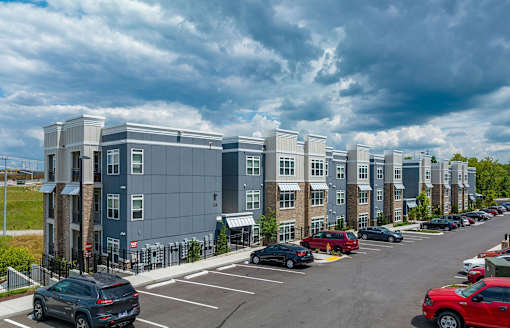 A row of modern apartment buildings with cars parked in the lot.