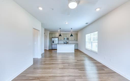 an empty open-concept living room and kitchen with white walls and wood floors