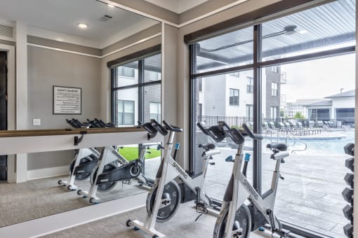 a gym with exercise bikes and a window view of a pool