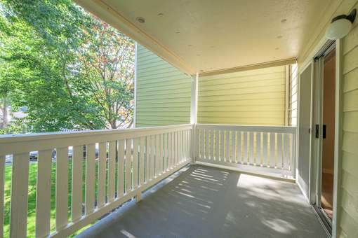 A white porch with a sliding door and a green tree in the background.