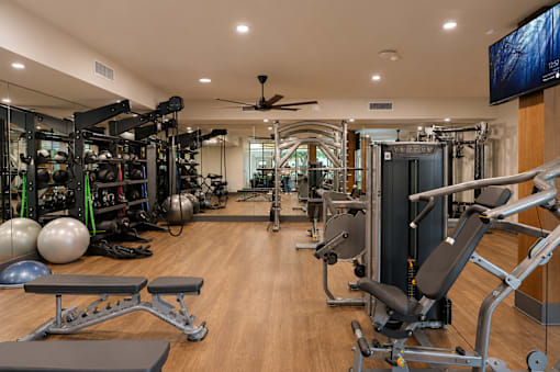 A spacious gym with a variety of equipment and a flat screen TV mounted on the wall.
