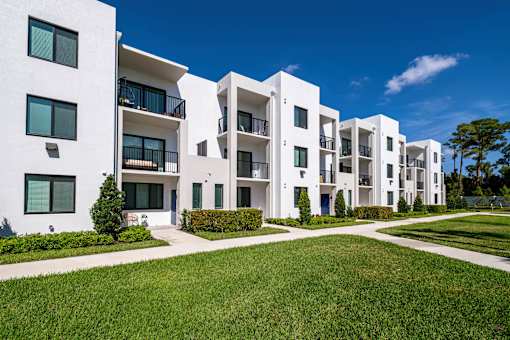 A row of white apartment buildings with green lawns in front.