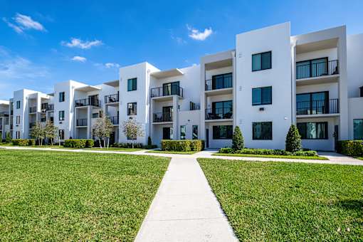A row of white apartment buildings with green lawns in front.