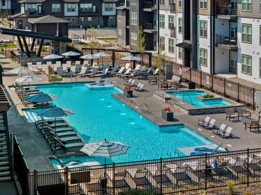 a swimming pool at an apartment complex with chairs and umbrellas