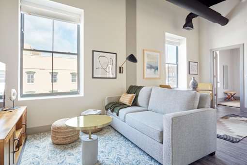 A living room with a grey couch, a round glass table, and a ceiling fan.