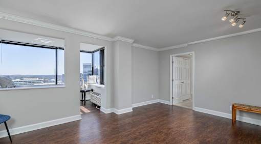 A room with a window overlooking a cityscape and a wooden floor.