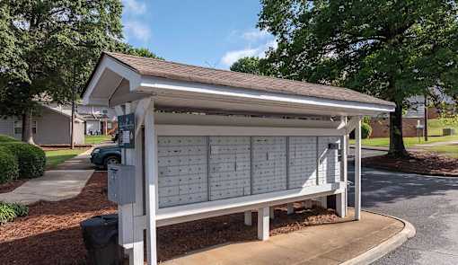A white wooden bench with a white roof is in front of a building.