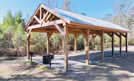 A wooden pavilion with a metal roof is surrounded by trees.