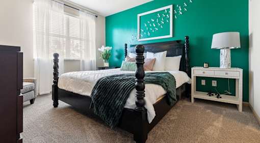 Luxury Apartments Near Tampa International Airport in Tampa, FL - Mosaic Westshore - A modern bedroom with a vibrant emerald green accent wall, a black four-poster bed, and white textured bedding.