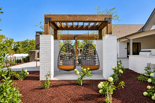A white house with a wooden pergola and a swing hanging from it.