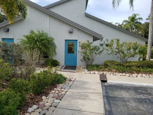 a white building with a blue door and a walkway with plants and trees at L'Estancia, Sarasota, 34231
