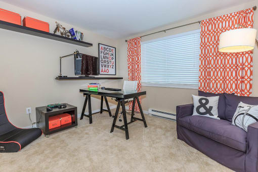 a living room with a couch and a desk in front of a window
