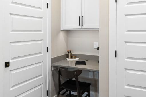 a small desk with two chairs in a room with white cabinets