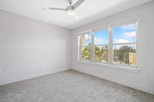 A room with a ceiling fan and a window overlooking a cityscape.