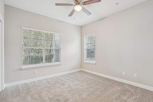 A room with a ceiling fan and two windows.