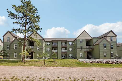 Apartment complex with a green building and a tree in front.