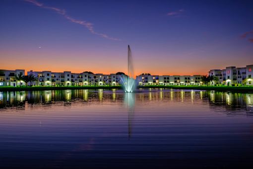 A fountain in the middle of a body of water with buildings in the background.