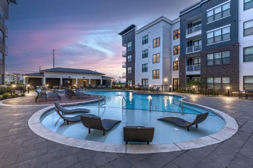 an apartment swimming pool with chairs at dusk