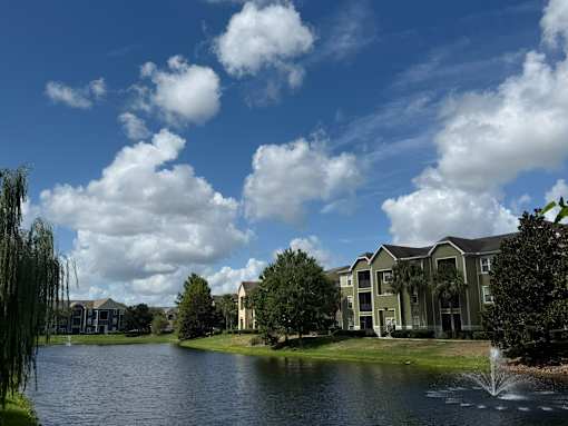 A large building is situated by a lake with a fountain in front of it.