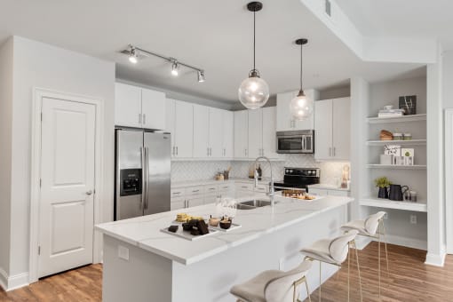 Buckhead, GA, Luxury Apartments Near Chastain Park - 92 West Paces - Modern Kitchen with Hardwood Flooring, White Maple Cabinetry with Stainless Steel Pulls, White Quartz Countertops, Large Cooking Island/Breakfast Bar, Bar-Style Chairs, Pendant and Track Lights, Stainless Steel Appliances, and Display Shelves.