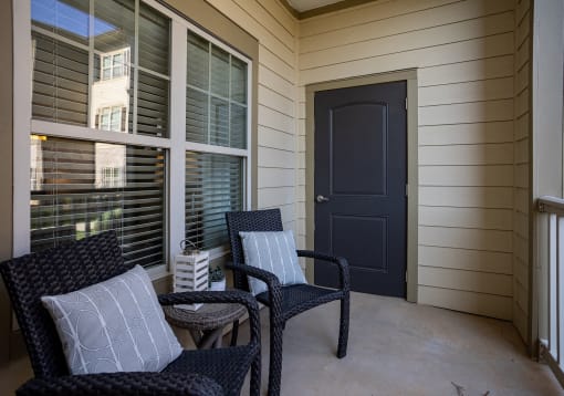 the front porch of a home with two chairs and a black door