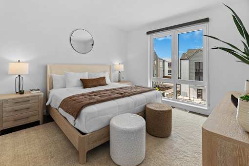 Two Bedroom Townhomes in Bozeman, MT - Highmark Bozeman - Bedroom With Area Rug, Bed, Nightstands With Lamps, Ottoman Stools, Dresser, And Floor-To-Ceiling Window.