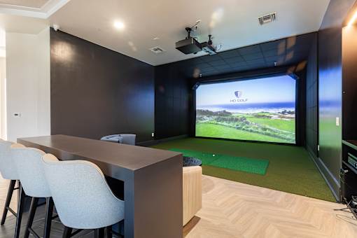 A room with a long table and chairs and a screen showing a golf course.
