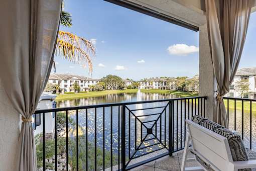 A balcony with a chair and a view of a lake and houses.