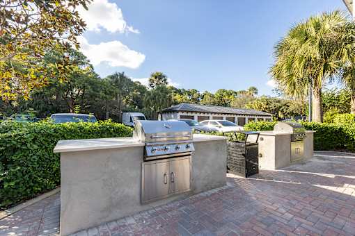 A brick patio with a grill and a wall in front of a tree.