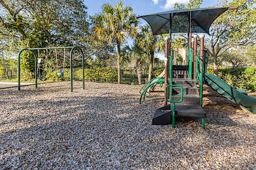 A playground with a green slide and a black and green swing set.