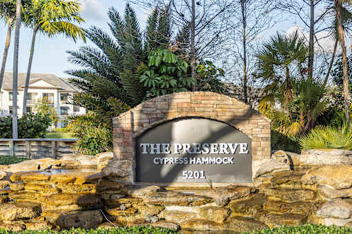 A sign that says "The Preserve Cypress Hammock 5201" is in front of a stone wall and palm trees.