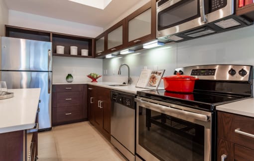 Orlando, FL Pet-Friendly Luxury Apartments - NORA - Kitchen with Moveable Island, Stainless Steel Appliances, Wood-Tone Cabinetry, and White Granite Countertops.