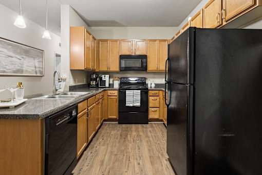 A black refrigerator is in the corner of a kitchen with wooden cabinets.