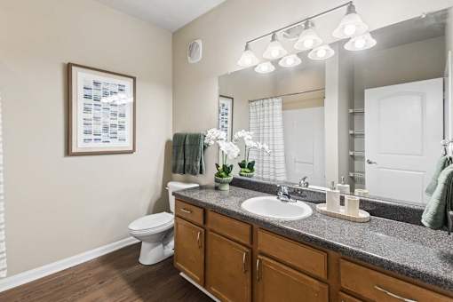 A bathroom with a toilet, sink, mirror, and a vase of flowers.