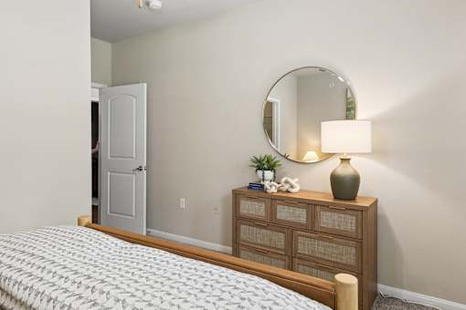 A bedroom with a bed, dresser, mirror, and lamp.