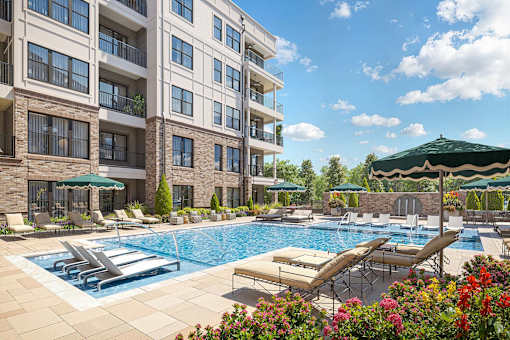 A large swimming pool with sun loungers and umbrellas in front of a multi-story apartment building.