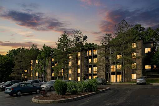 A parking lot with cars and a building with windows and trees in front at Winchell Way Apartment , Kalamazoo, 49008