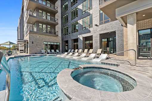 A large outdoor swimming pool with a hot tub in the middle of it.