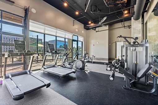 Pet-Friendly Luxury Apartments in Huntsville, AL - The Arcadia - Fitness Center with Treadmills, Elliptical Machines, Stationary Bike, Weight Lifting Equipment, High Ceiling with Exposed Piping, Ceiling Fan, and Window Wall with View of Pool Area.