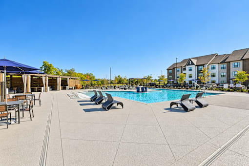 A large outdoor swimming pool with sun loungers and a building in the background.