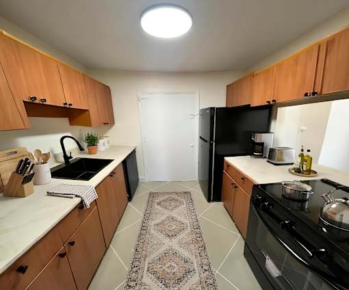 Dog-Friendly Luxury Apartments In Hollywood, FL - Park Hill Hollywood - A Modern Kitchen With Tile Flooring, Wood Cabinetry, Granite Countertops, And Black Appliances.