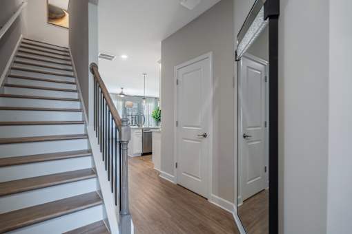 A staircase with a wooden handrail and steps leads to a brightly lit room with white doors.