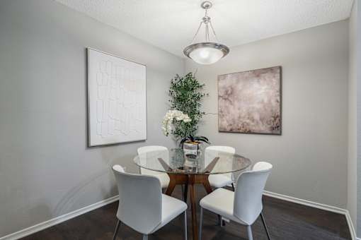 A dining room with a glass table and white chairs.