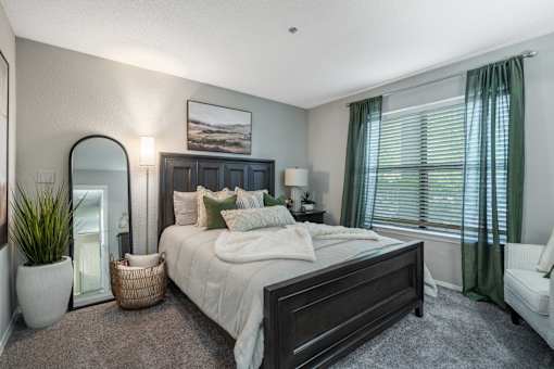 A bedroom with a large bed, a mirror, a potted plant, and a painting on the wall.
