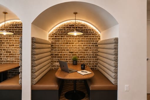A room with a brick wall and a table with a laptop and a mug on it.