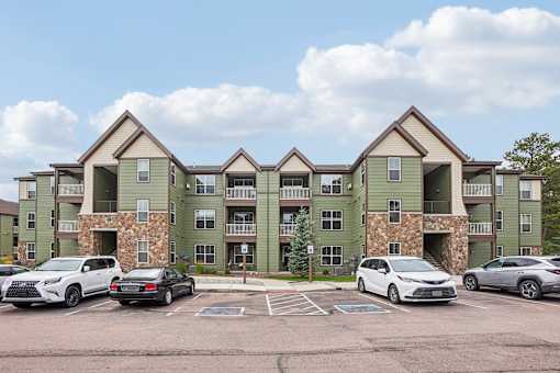 A row of apartment buildings with cars parked in front.