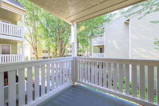 A white balcony with a railing overlooking a green area.